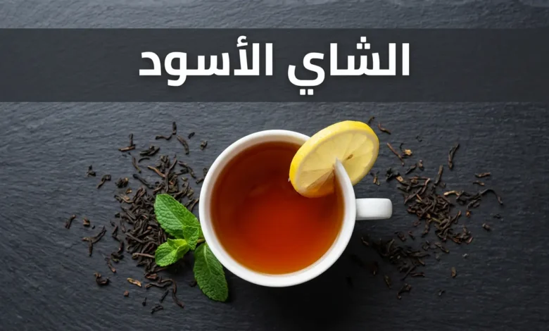 كوب شاي أسود داكن اللون بجانب أوراق شاي جافة وشريحة ليمون على سطح حجري