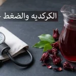 إبريق زجاجي مليء بمشروب الكركديه الأحمر بجانب جهاز قياس ضغط الدم على سطح داكن