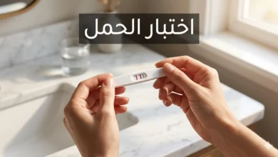 يدان تمسكان شريط اختبار حمل منزلي يُظهر خطين وردييَن على خلفية رخام أبيض في إضاءة صباحية طبيعية