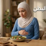 صورة غلاف لمقال طبي عن غازات البطن تُظهر امرأة شابة تضع يدها على بطنها بجانب وجبة صحية على طاولة طعام