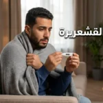 رجل عربي شاب يجلس على أريكة ملفوفاً ببطانية خفيفة ويمسك ميزان حرارة رقمي مع ظهور عبارة أسباب القشعريرة