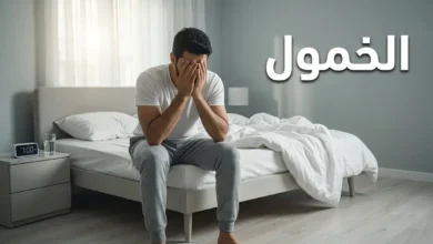 رجل عربي شاب يجلس على حافة السرير صباحاً ممسكاً رأسه بيديه في حالة خمول وإرهاق رغم النوم الطويل