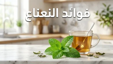 أوراق نعناع فلفلي طازجة مع كوب شاي نعناع ساخن على سطح رخامي أبيض وعنوان فوائد النعناع