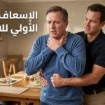 رجل يُطبّق مناورة هيمليك على شخص بالغ يختنق في غرفة طعام منزلية، مع توضيح وضعية اليدين الصحيحة فوق السرّة مباشرة — الإسعاف الأولي للاختناق