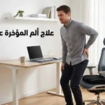 رجل يقف من كرسي مكتبه الأرغونومي وهو يضع يده على مؤخرته بألم خفيف مع وسادة عصعص طبية على الكرسي وعنوان علاج ألم المؤخرة عند الجلوس