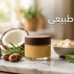 برطمان زجاجي أنيق يحتوي على بلسم طبيعي ذهبي محاط بمكس أرغان وجوز هند ولافندر وزبدة شيا وألوفيرا على سطح رخامي بإضاءة طبيعية