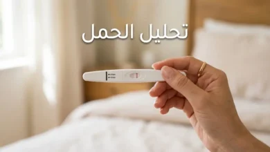 يد تمسك شريط اختبار حمل منزلي يُظهر نتيجة إيجابية بخطين وردييْن
