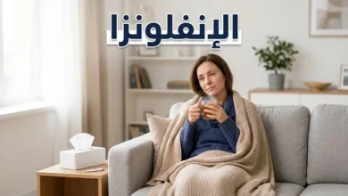 شخص بالغ يرتاح في المنزل أثناء إصابته بالإنفلونزا مع كوب شاي دافئ ومنديل وترمومتر